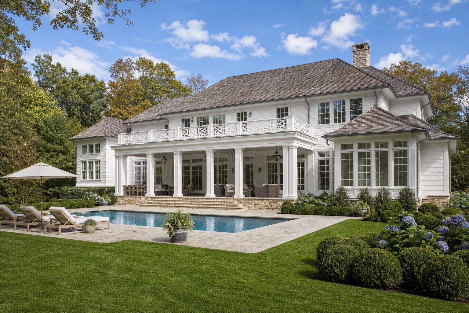 Colonial Revival estate rear elevation after renovation with rectangular swimming pool, stone pool deck, covered terrace, lounge seating, and hydrangea planting in Greenwich
