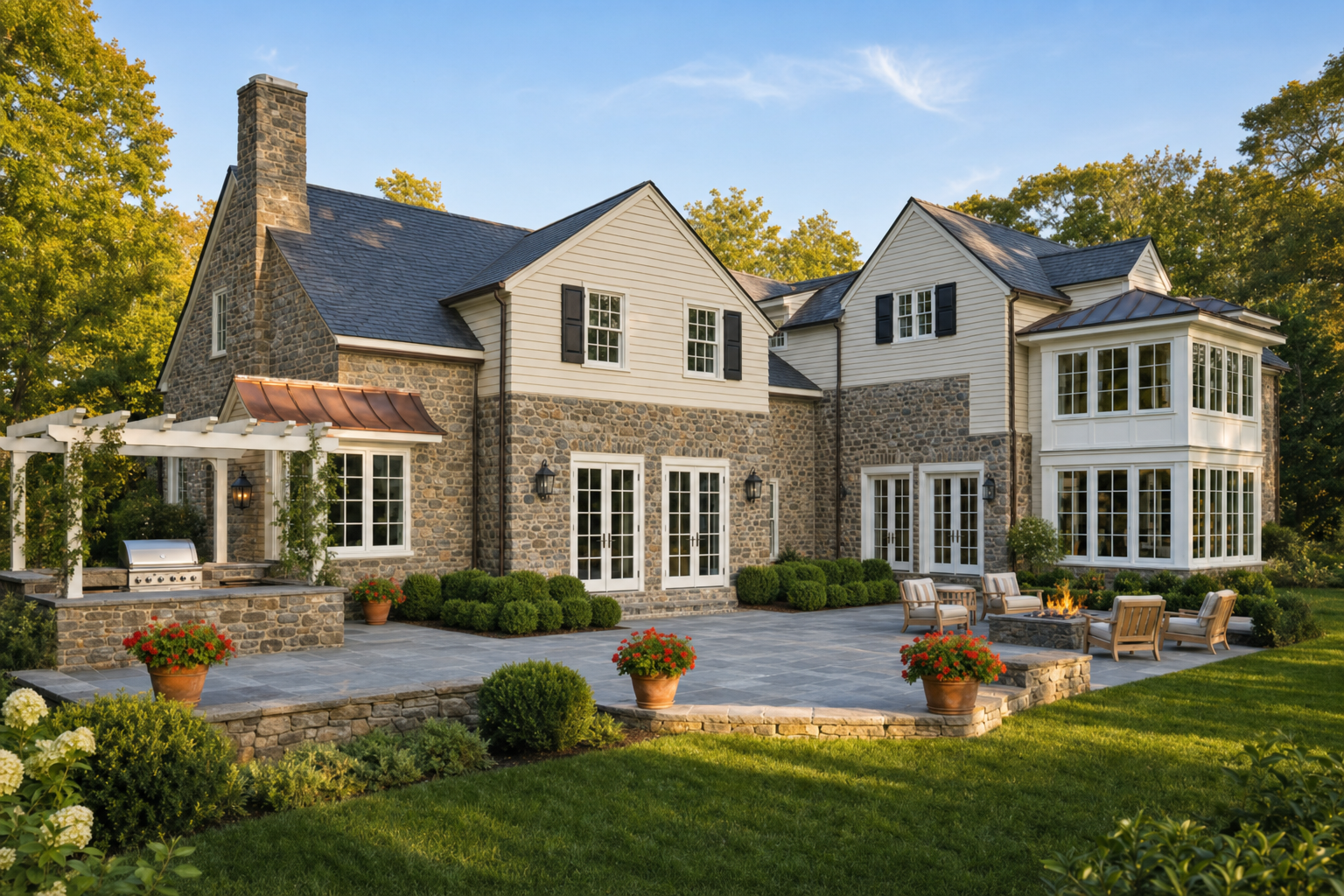 Fieldstone estate rear elevation before screened porch addition, with French doors to bluestone terrace, outdoor kitchen pergola, fire pit, and boxwood hedges in Greenwich