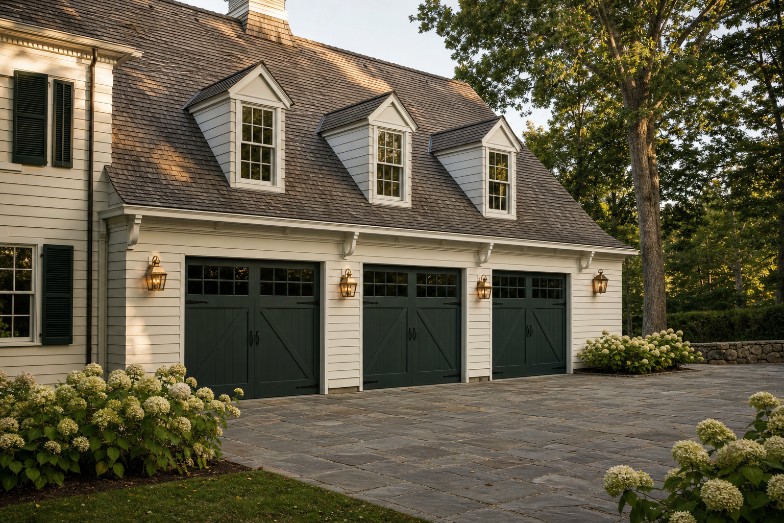 Three-car garage with white clapboard, green carriage doors, brass lanterns, bluestone drive, and hydrangea borders in Greenwich