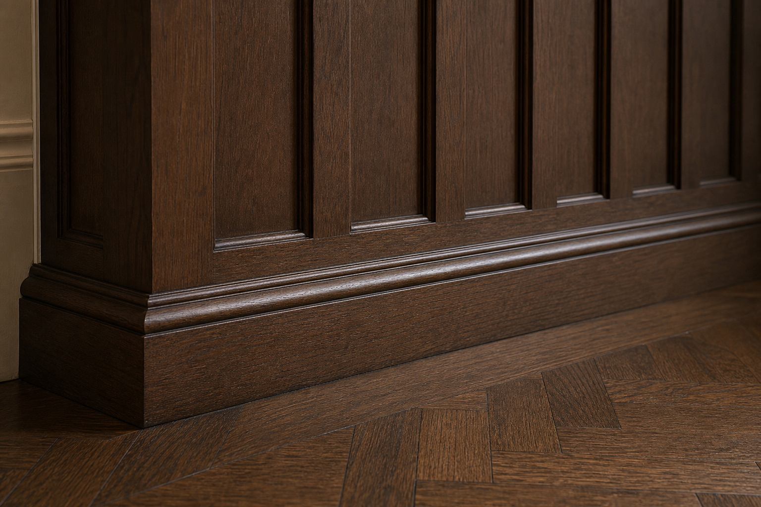 Close-up of tiered walnut baseboard meeting dark herringbone parquet floor at the base of Craftsman board-and-batten wainscoting in Greenwich